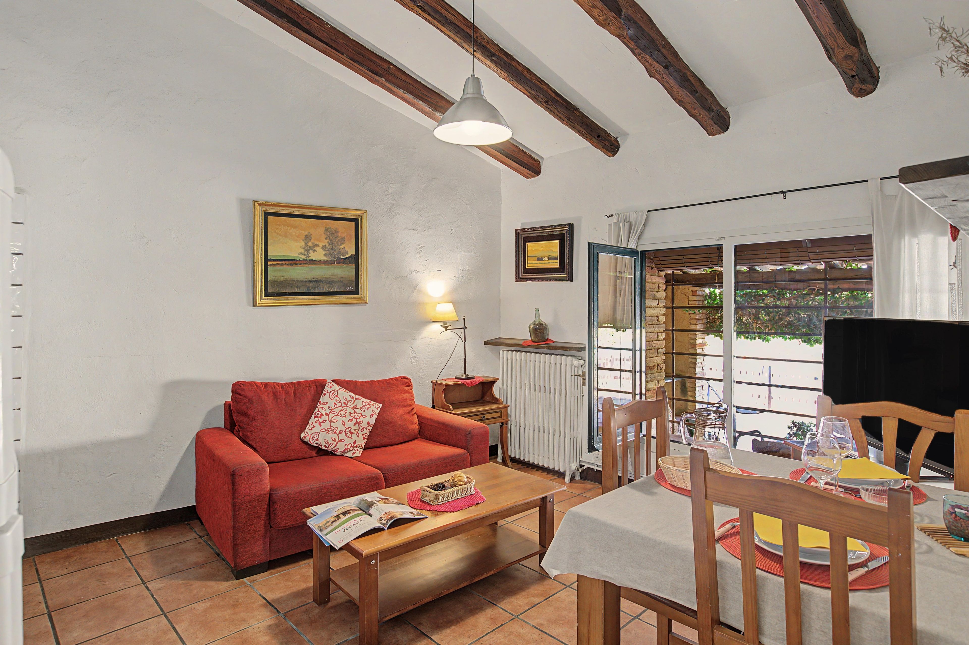 A cozy living room with a red sofa, a wooden coffee table, and a dining area with a table set for two.