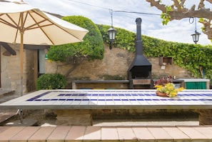 An outdoor patio with a tiled table, a barbecue grill, and a pergola with a canopy. - Two 18th-century country houses 'Can Gat Vell' with private pool, Wi-Fi, AC, fans (LLAMPAIES)