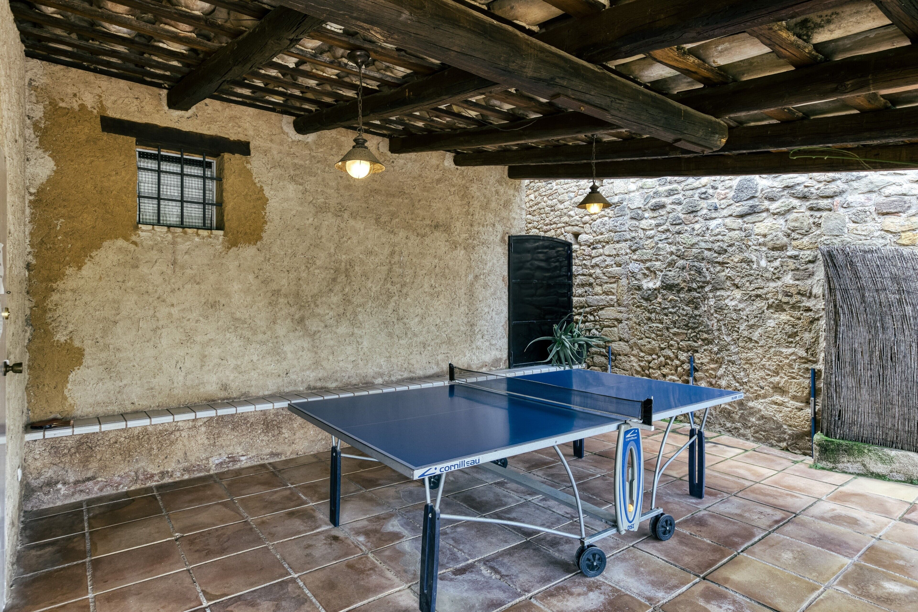 A ping pong table in an outdoor area with stone walls and a wooden ceiling.