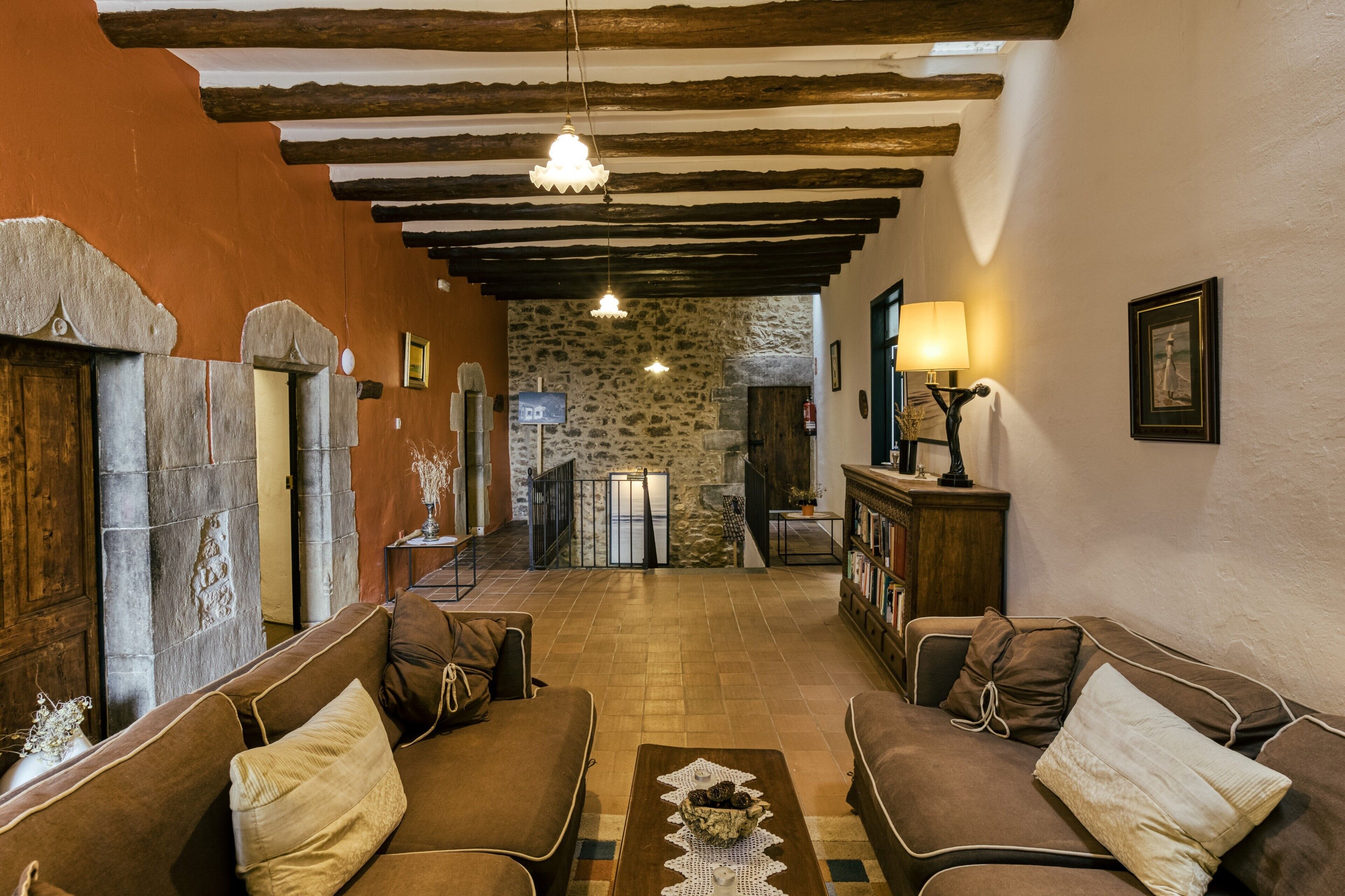 A cozy interior with a stone wall, wooden beams, and a fireplace. There are two sofas and a coffee table with decorative items.
