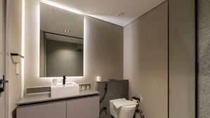 A modern bathroom with a large mirror, a white sink, a toilet, and a trash can. - MAG EYE 890 - Modern Studio Near Downtown (Meydan)
