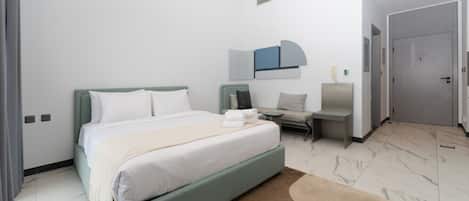 Une chambre d’hôtel moderne comprenant un lit, un coin salon et une porte donnant sur une autre pièce.