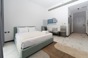 A modern hotel room with a bed, a seating area, and a door leading to another room. - MAG EYE 890 - Modern Studio Near Downtown (Meydan)
