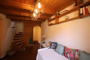 A bedroom with a wooden ceiling, a bed with a white bedspread, a floral pillow, a bedside table with a vase, and a staircase with a wooden railing. - Casa Holamundo, authentic 1900 Stone House in the Mountains near Lugano (Curtina)