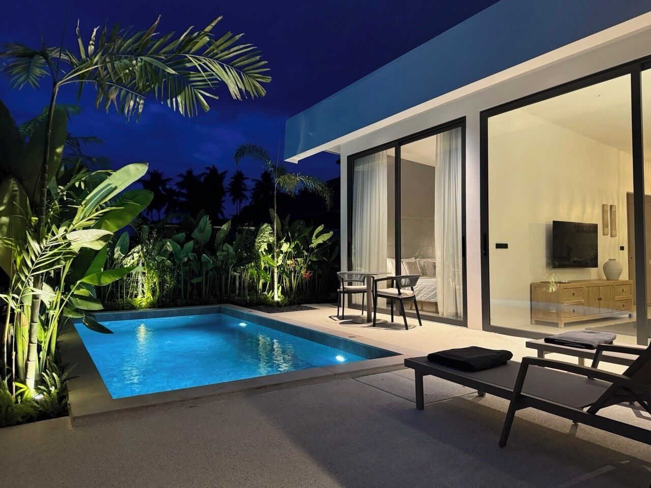 A modern outdoor pool area with a glass-enclosed room, a sofa, and a TV.