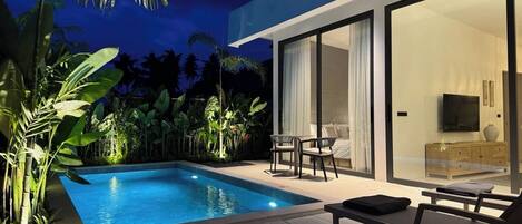 A modern outdoor pool area with a glass-enclosed room, a sofa, and a TV.