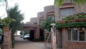 A gated entrance with a paved driveway leading to a building with multiple windows and a covered walkway. - Dalmia Resort - Puri (Puri)