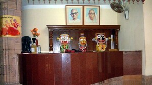 A reception desk with framed photographs above, a fan on the wall, and a statue on the left.