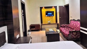 Una camera d'albergo con un letto, un divano, una TV a muro, una ventola a soffitto e un tavolino.