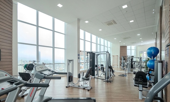 A gym with cardio equipment, weight machines, and a view of the city.
