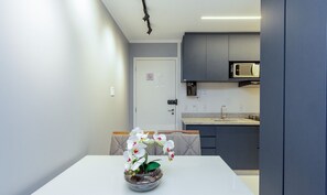 A compact kitchen with grey cabinets, a microwave, and a sink. There's a white table with a vase of white flowers. - Equipped apt Near the Mall - Wbu2607 (Goiânia)