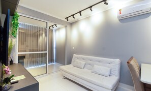 A modern living room with a white sofa, a glass door leading to a balcony, and an air conditioning unit on the wall.