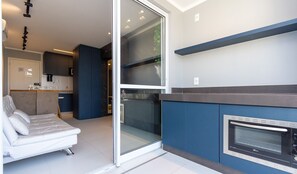 Een moderne keuken met een inbouwoven, een zithoek met een bank, en een schuifpui naar een balkon.