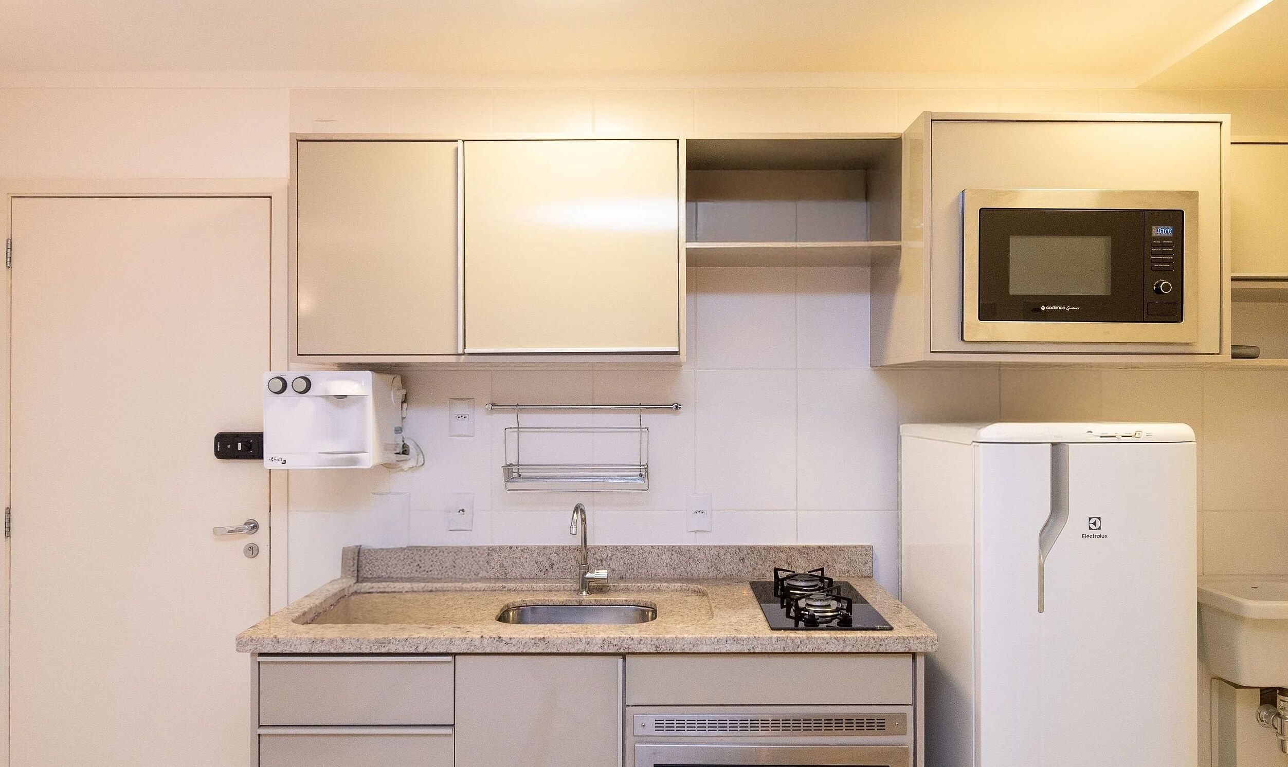 Een compacte kitchenette met een ingebouwde magnetron, een kleine koelkast, een koffiezetapparaat en een gasfornuis.