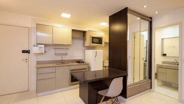 A modern kitchen with a built-in microwave, refrigerator, and a small dining area with a chair. - Flat w/ gym in Setor Bueno - Wbu2405 (Goiânia)
