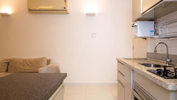 Cocina compacta con estufa integrada, lavamanos y microondas. Cuenta con una pequeña zona de estar con un sofá y una silla.