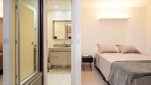 A bedroom with a bed, bedside table, and a bathroom with a sink and mirror. - Flat w/ gym in Setor Bueno - Wbu2405 (Goiânia)
