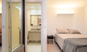 A bedroom with a bed, bedside table, and a bathroom with a sink and mirror. - Flat w/ gym in Setor Bueno - Wbu2405 (Goiânia)