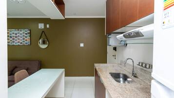 Cocina compacta con encimera de granito, pileta de acero inoxidable y refrigerador blanco.