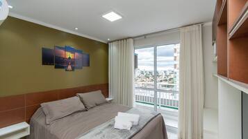 A hotel room with a bed, a window with curtains, and a cityscape view.