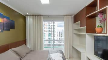 A hotel room with a bed, a TV, a balcony with curtains, and a city view.