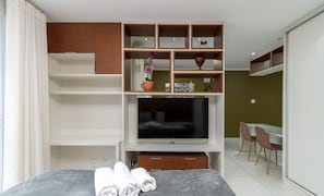 A modern hotel room with a bed, a TV, a desk, and a seating area.