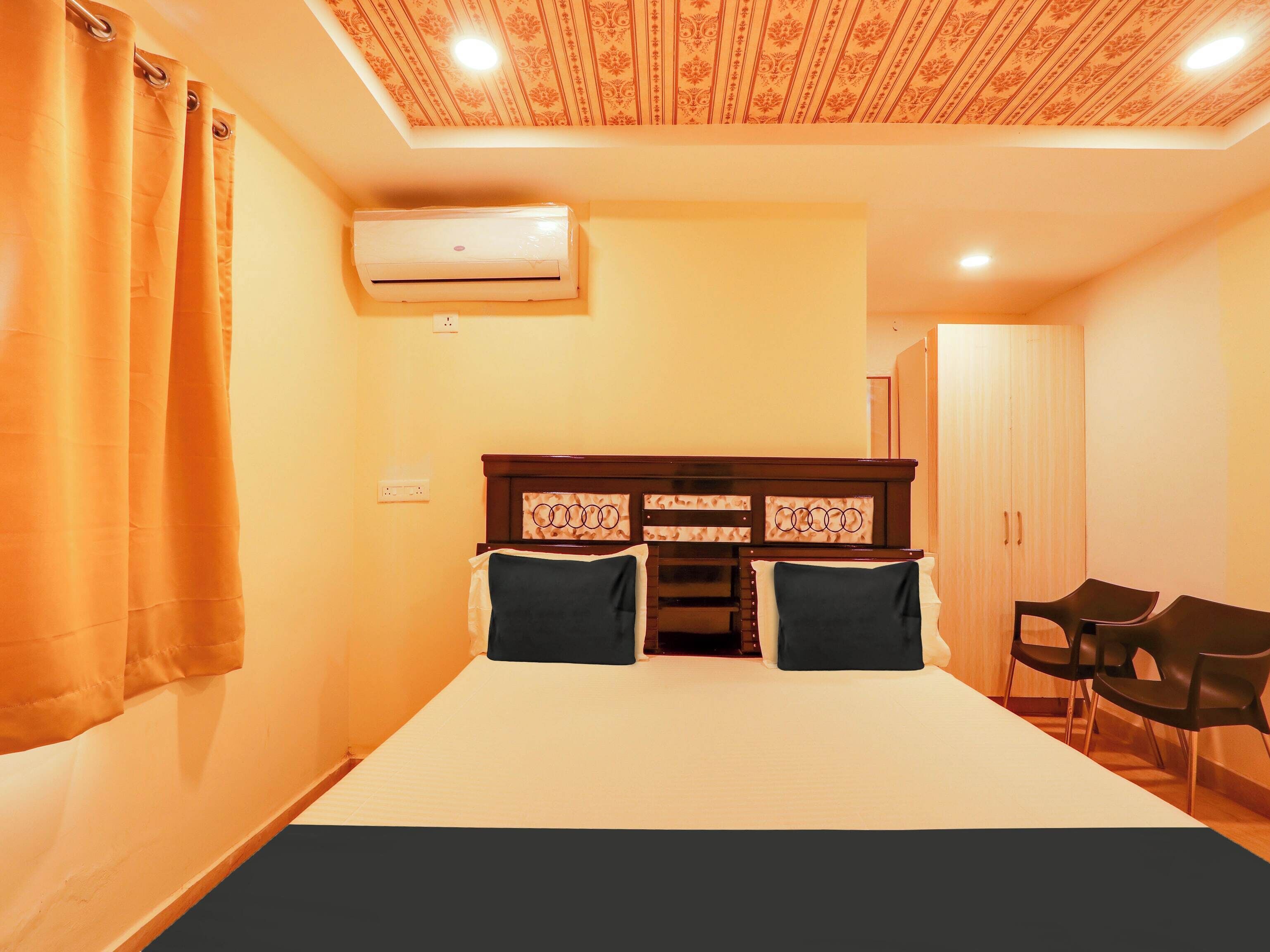Habitación de hotel con una cama, dos almohadas, cabecero con panel decorativo, unidad de aire acondicionado, armario y dos sillas.