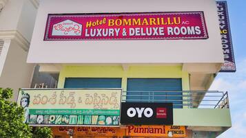 Un hotel llamado Hotel Bommarillu, con carteles que indican habitaciones de lujo y superiores, una agencia Punnami Agro, y un cartel de OYO Hotel.