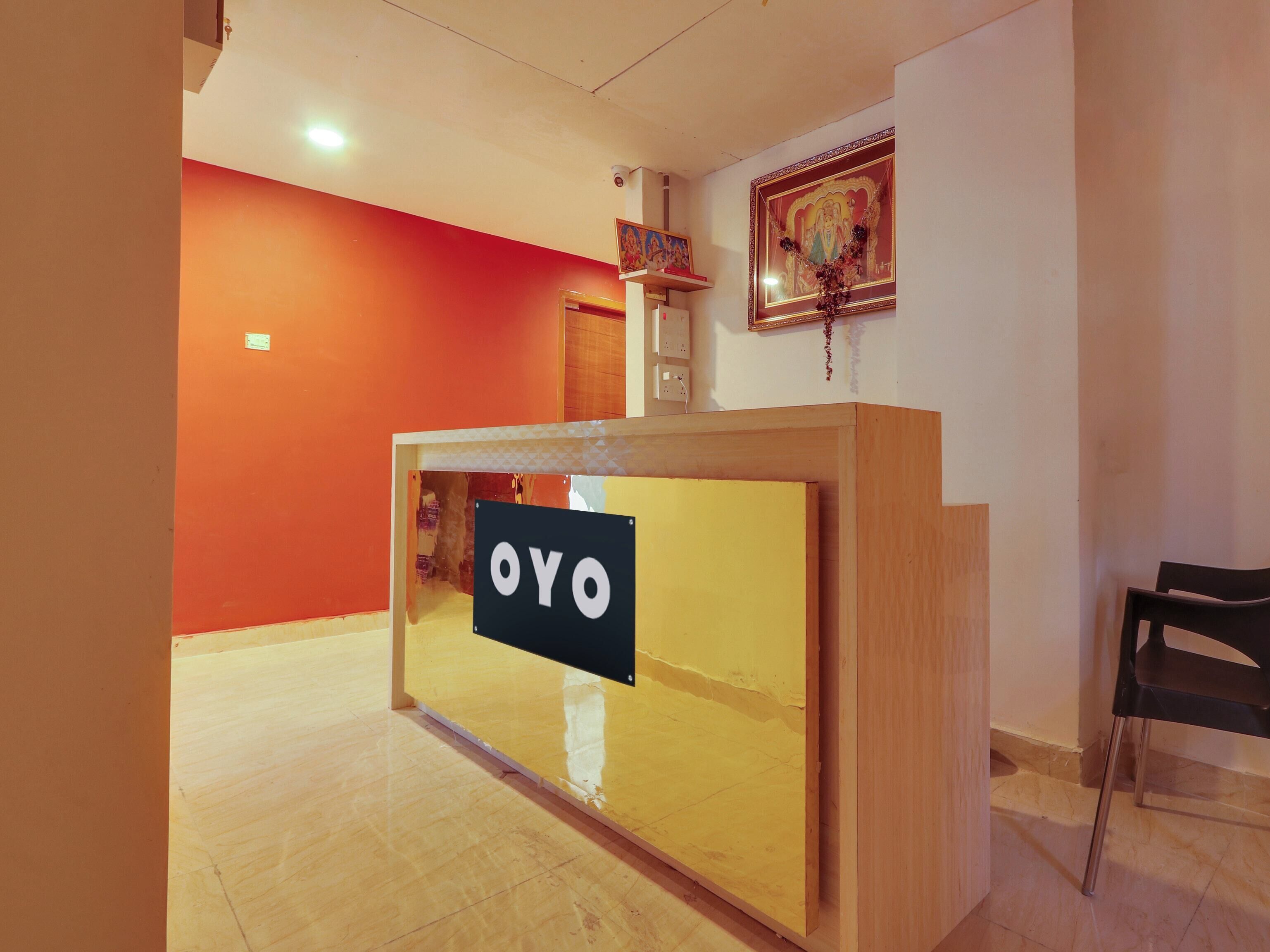 A reception desk with a sign that reads 'OYO' in a hotel lobby with orange walls and a wooden floor.