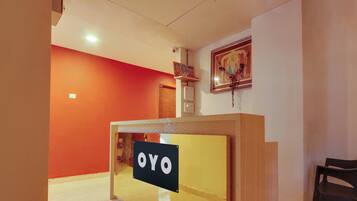 A reception desk with a sign that reads 'OYO' in a hotel lobby with orange walls and a wooden floor.
