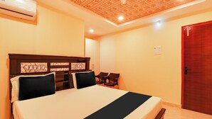 A hotel room with a bed, a ceiling fan, an air conditioning unit, a door, and a small table.