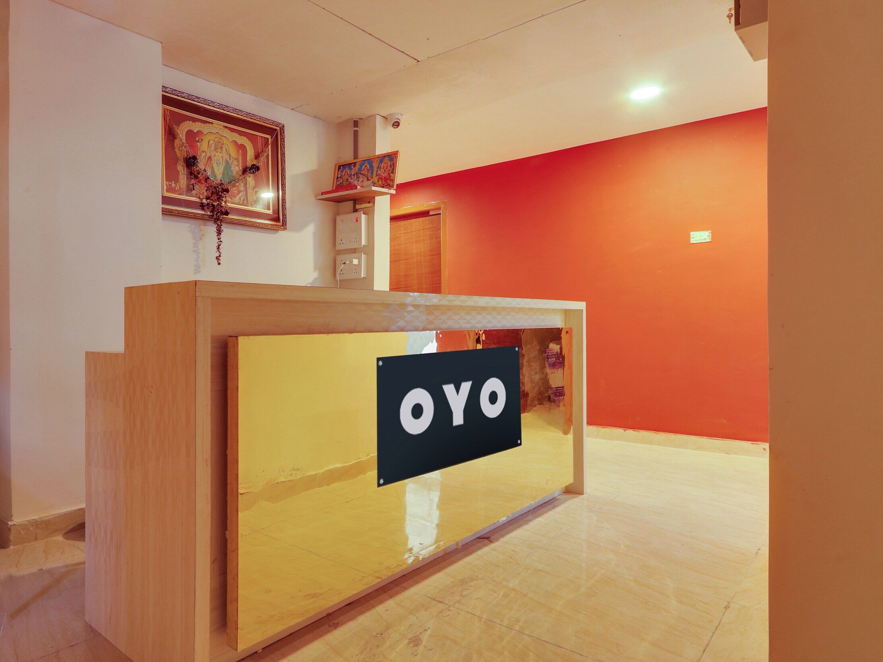 Un mostrador de recepción con un letrero que dice 'OYO' en el vestíbulo de un hotel con una pared roja y un cuadro enmarcado sobre el mostrador.