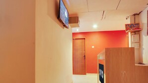 A hotel corridor with a reception desk, a television mounted on the wall, and a wooden door at the end.