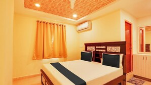 A hotel room with a bed, a ceiling fan, an air conditioning unit, and a wooden wardrobe.