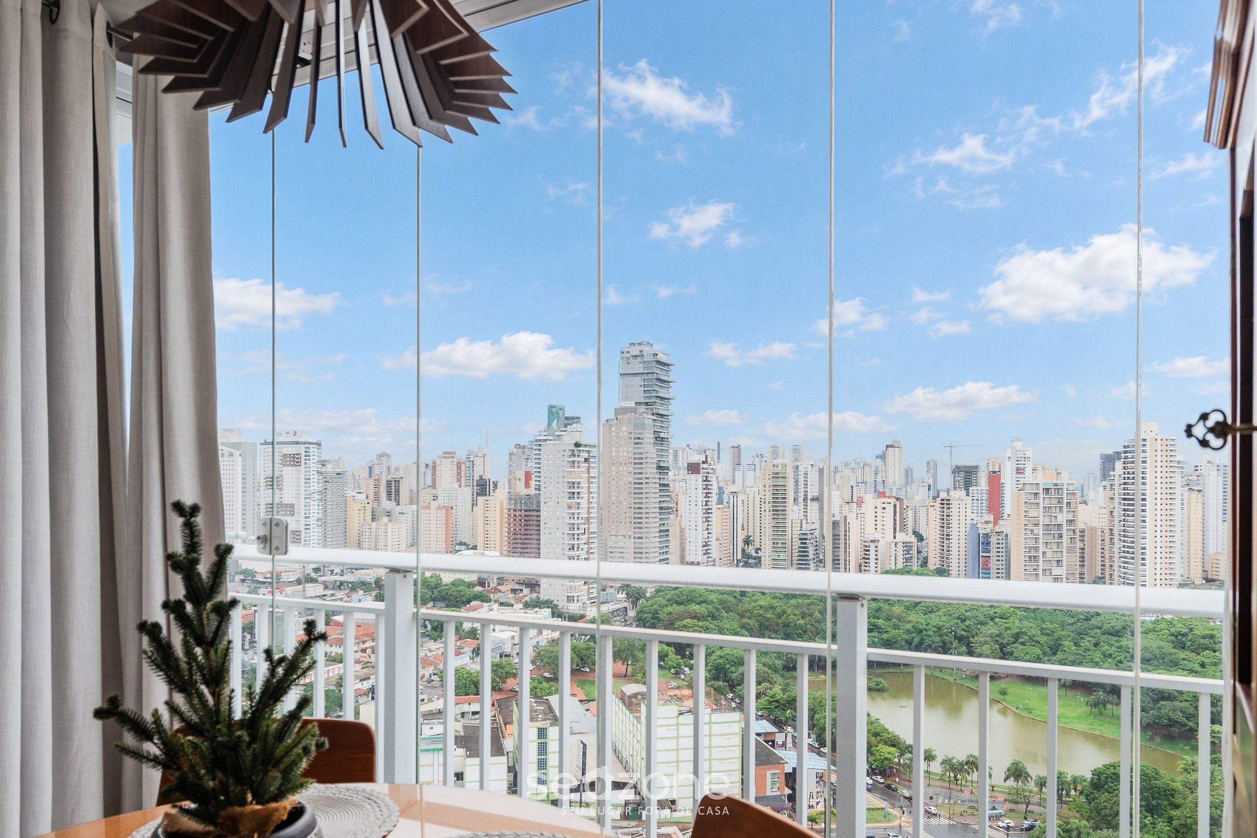 Un balcon avec vue sur la ville, une plante en pot et un luminaire suspendu.