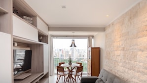 Een moderne woonkamer met een eethoek, een televisie en uitzicht op een stadsbeeld door een groot raam.