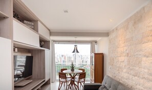 Ein modernes Wohnzimmer mit Essbereich, Fernseher und Blick auf eine Stadtlandschaft durch ein großes Fenster.