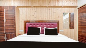 A room with a wooden paneled wall, a tufted headboard, a bed with white bedding and two black pillows, and a wooden wardrobe. - Collection O Tajganj West Gate (Agra)