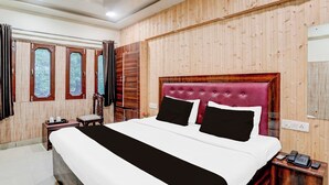 A hotel room with a large bed, wooden panel walls, a wooden nightstand with a phone, and a window with curtains. - Collection O Tajganj West Gate (Agra)