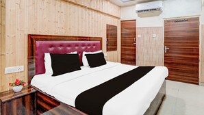 A hotel room with a wooden paneled wall, a tufted headboard, a bed with white bedding and black accents, a nightstand with a vase of flowers, and a wooden wardrobe. - Collection O Tajganj West Gate (Agra)