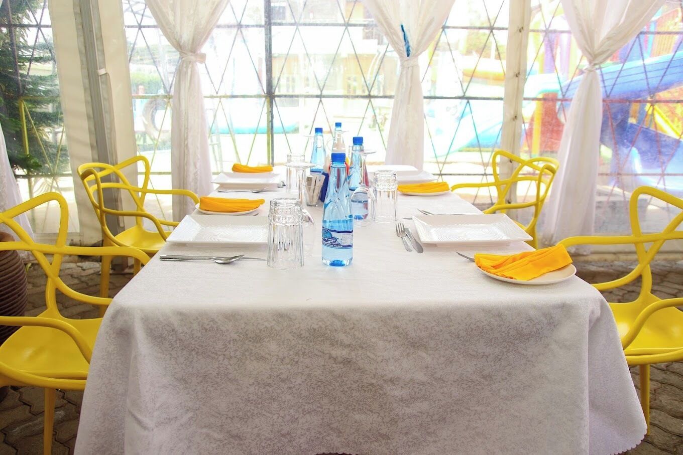 Mesa para dos con sillas amarillas, mantel blanco y una botella de agua.
