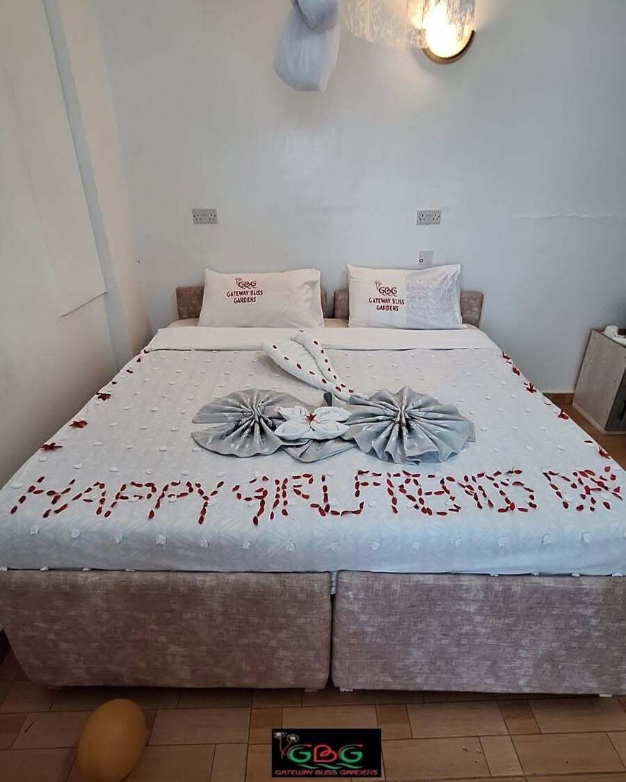 A neatly made bed with a message towel, two pillows with a logo, and a wall-mounted light fixture.