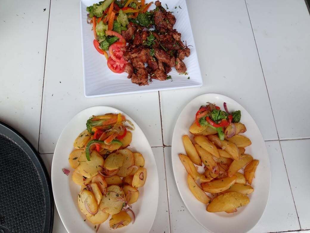 A dining table with two plates of food, one with a meat dish and vegetables, and the other with potato wedges and vegetables.