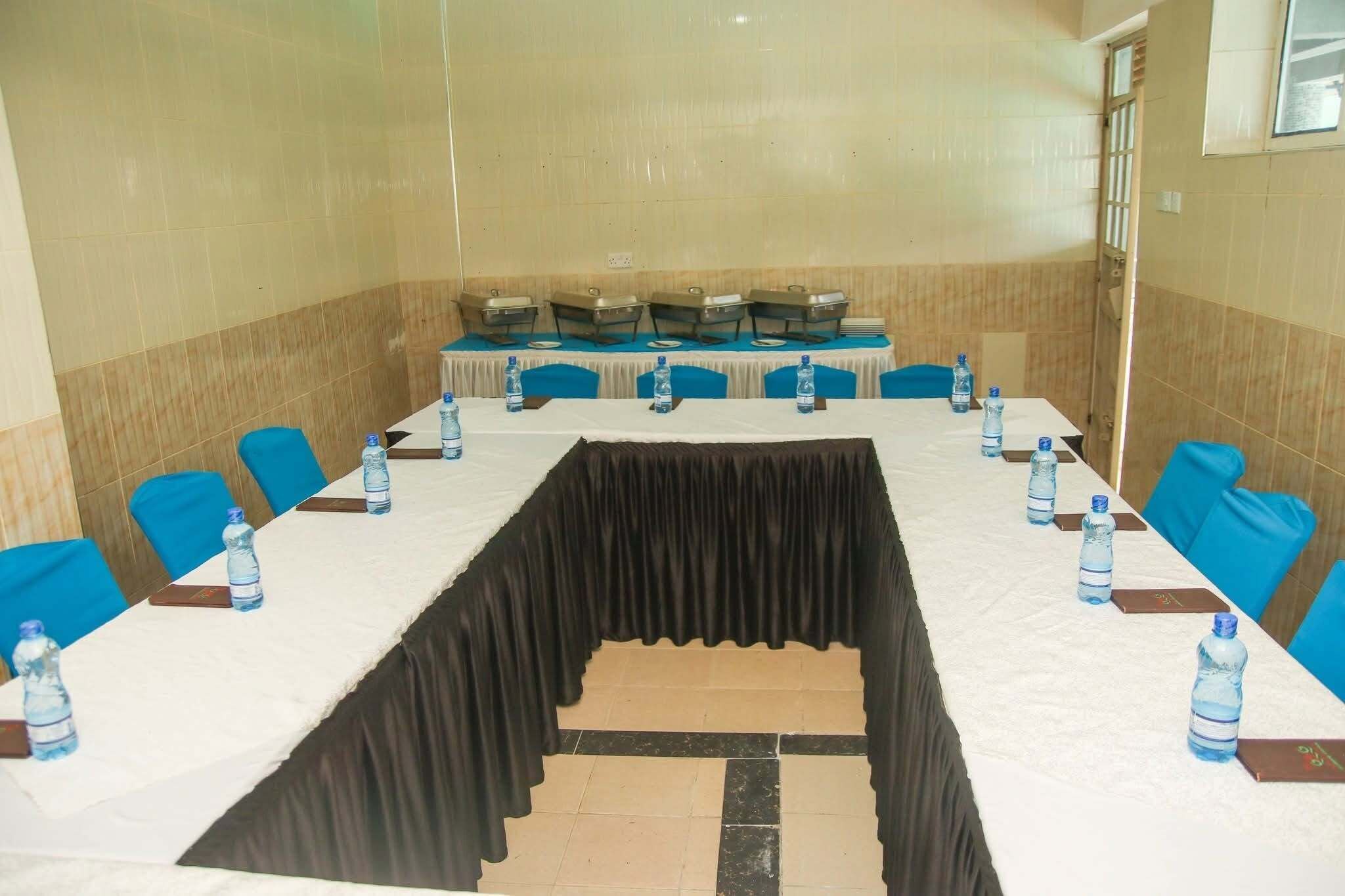 A conference room with a long table, blue chairs, water bottles, and a black curtain.