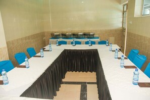 A conference room with a long table, blue chairs, water bottles, and a black curtain.