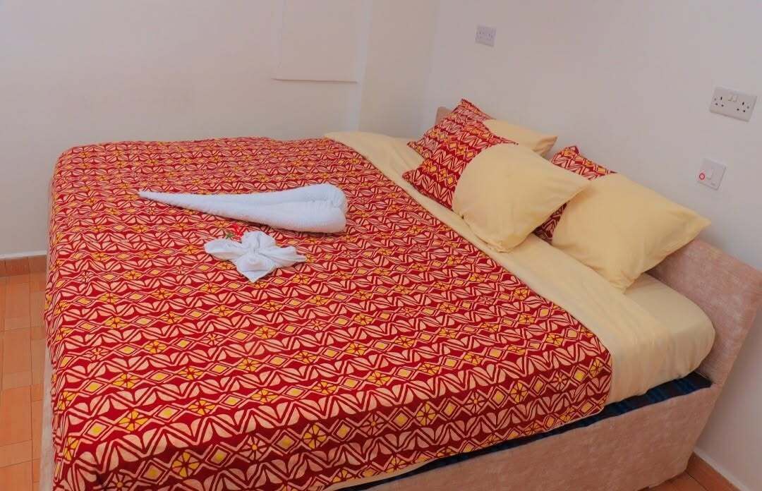 Una cama con una colcha estampada, una toalla blanca y dos almohadas.