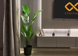 Un salon moderne avec une plante en pot, un tableau encadré et un téléviseur fixé au mur.