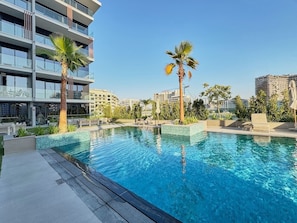 Ein Schwimmbecken mit klarem, blauem Wasser, umgeben von einem modernen Gebäude mit Balkonen und Palmen.