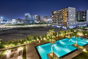A hotel with a pool area, multiple buildings in the background, and a well-lit outdoor space. - Chic Studio | Pool View Balcony | Avelon Arjan (Dubai)