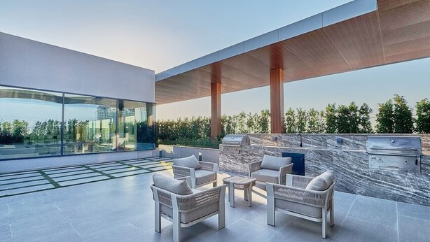 An outdoor patio with modern furniture, a grill, and a view of the cityscape. - Chic Studio | Pool View Balcony | Avelon Arjan (Dubai)